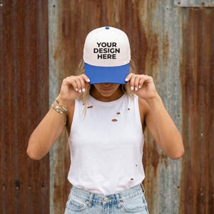 Könnte beinhalten: Eine weiß-blaue Baseballkappe mit dem Text "YOUR DESIGN HERE" in Schwarz. Die Kappe hat eine weiße Krone und einen blauen Schirm. Die Person auf dem Bild trägt ein weißes Tanktop und blaue Jeans.