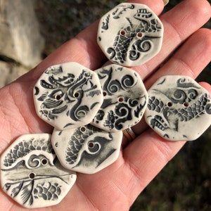 May include: Six white ceramic buttons with black ink designs of dragons and clouds. The buttons are octagonal in shape and have two holes.
