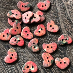 May include: A collection of 18 heart-shaped buttons with a red, orange, and green floral pattern. The buttons have two holes each.