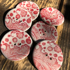 Può includere: Sei bottoni in ceramica bianca con un motivo floreale rosso. I bottoni hanno due fori ciascuno.