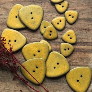 May include: A collection of 12 yellow triangle-shaped buttons with two holes each. The buttons are arranged in a random pattern on a wooden surface.