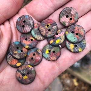 Op de afbeelding: Een verzameling kleurrijke, gepatroneerde knopen met elk twee gaten. De knopen zijn gemaakt van hout en hebben een verscheidenheid aan kleuren en ontwerpen, waaronder rood, blauw, groen, geel en zwart.