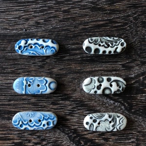 May include: Six ceramic buttons with blue and white or black and white floral patterns. The buttons are oval shaped and have two holes.