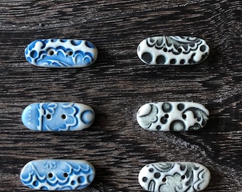 Könnte beinhalten: Sechs Keramikknöpfe mit blauen und weißen oder schwarzen und weißen Blumenmustern. Die Knöpfe sind oval geformt und haben zwei Löcher.