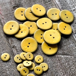 May include: A collection of yellow wooden buttons with two holes each. The buttons are arranged in a random pattern on a wooden surface.
