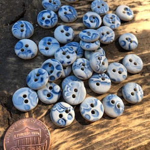 May include: A collection of blue and white ceramic buttons with a floral pattern. The buttons are arranged in a pile on a wooden surface.