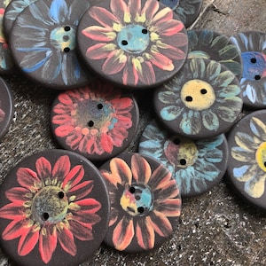 Może przedstawiać: Kolekcja ręcznie robionych ceramicznych guzików z kwiatowymi wzorami. Guziki są pomalowane w różnych kolorach, w tym czerwonym, niebieskim, żółtym i zielonym. Guziki są okrągłe i mają wypukły wzór.