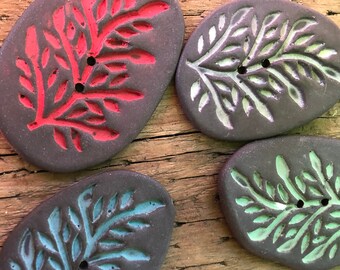 May include: Four ceramic buttons with a dark brown background and a white, green, or red leaf design. The buttons have two holes each.