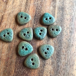 May include: Nine triangular ceramic buttons in shades of green and brown with three holes each.