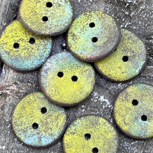 Peut inclure: Un ensemble de huit boutons ronds, jaunes et bleus, avec deux trous chacun. Les boutons ont une surface texturée et mouchetée et sont disposés en grappe.