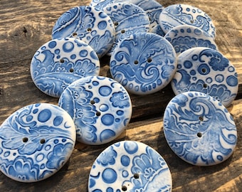 Könnte beinhalten: Eine Sammlung von 12 Keramikknöpfen mit einem blauen und weißen Paisley-Muster. Die Knöpfe sind rund und haben zwei Löcher.