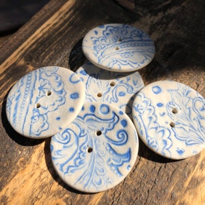 Peut inclure: Cinq boutons en céramique avec un motif floral bleu et blanc. Les boutons sont ronds et ont deux trous chacun.