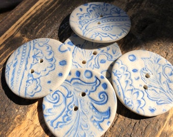 Könnte beinhalten: Fünf Keramikknöpfe mit einem blauen und weißen Blumenmuster. Die Knöpfe sind rund und haben jeweils zwei Löcher.