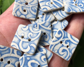 Könnte beinhalten: Eine Sammlung von blauen und weißen Keramikknöpfen mit einem wirbelnden Muster. Die Knöpfe sind quadratisch und haben jeweils zwei Löcher.