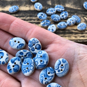 May include: A collection of oval-shaped ceramic buttons with a blue and white floral pattern. The buttons are arranged in a hand, with some buttons overlapping.