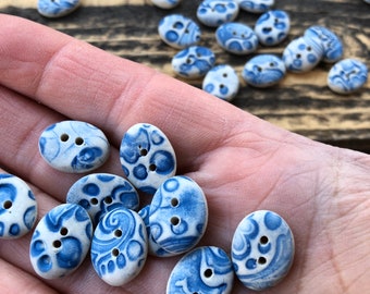 May include: A collection of oval-shaped ceramic buttons with a blue and white floral pattern. The buttons are arranged in a hand, with some buttons overlapping.