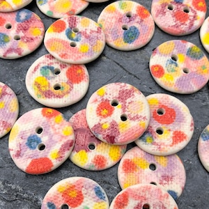 May include: Assortment of colourful, round buttons with a white background and a floral pattern. The buttons have two holes and are made of ceramic.