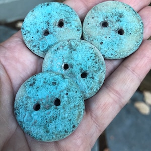 May include: Four teal blue ceramic buttons with a speckled pattern and two holes each.