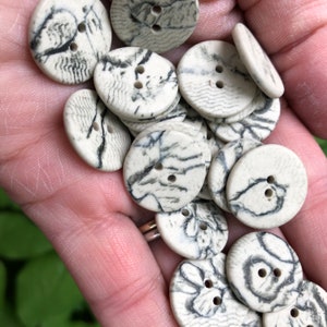 May include: A pile of white ceramic buttons with black marbling. The buttons have two holes each.