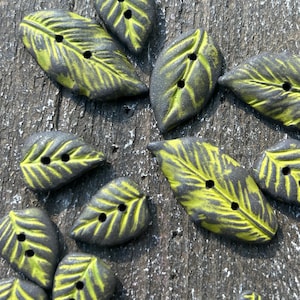 Peut inclure: Un ensemble de 10 boutons en forme de feuille avec un motif noir et vert. Les boutons ont deux trous chacun et sont en céramique.