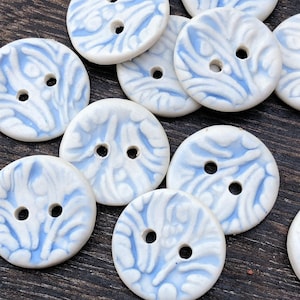May include: A collection of white ceramic buttons with a blue swirl pattern. The buttons have two holes each.
