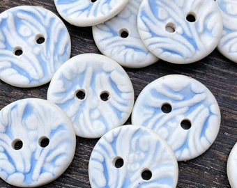 May include: A collection of white ceramic buttons with a blue swirl pattern. The buttons have two holes each.