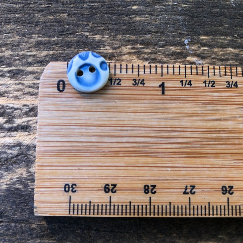 May include: A blue and white ceramic button with two holes. The button is approximately 1/2 inch in diameter.