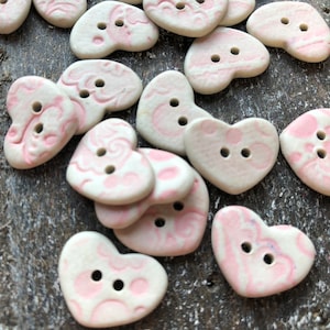 Peut inclure: Une collection de boutons en céramique en forme de cœur, de couleur rose et blanche, avec un motif en spirale.