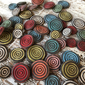 May include: A collection of colourful ceramic coasters with concentric circles. The coasters are in various colours, including red, blue, green, yellow, and black. They are arranged in a random pattern on a wooden surface.