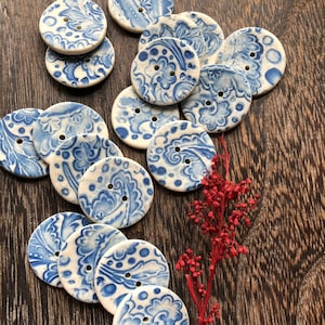Op de afbeelding: Een verzameling van 14 keramische knopen met een blauw en wit bloemenpatroon. De knopen zijn in een cirkel op een houten oppervlak gerangschikt.