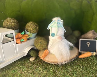 Puede incluir: Un camión de juguete blanco transporta zanahorias naranjas y bolas de musgo. Un gnomo blanco con una larga barba blanca y un sombrero azul y verde está sentado en una rodaja de madera. Una pequeña pizarra muestra el número 9.