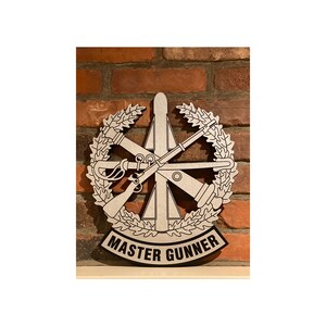 May include: A silver metal plaque with a wreath of leaves and crossed rifles, a rocket, and the text "MASTER GUNNER".