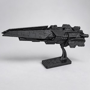 May include: A matte black plastic model of a futuristic starship featuring intricate paneling and mechanical details. The vessel is mounted on a rectangular display stand that includes a molded emblem on its base, showcasing a sharp, angular design.
