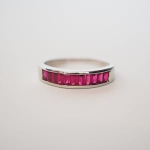 May include: A silver band ring with a row of red ruby stones.