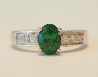 May include: A silver ring featuring a green oval gemstone set in a band of smaller white gemstones.