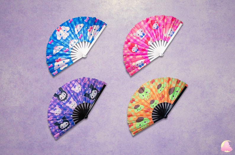 May include: Four hand fans with different cartoon character designs. The fans are made of fabric and have a white or black handle. The designs include a blue fan with white clouds and pink bows, a pink fan with white hearts and pink bows, a purple fan with white stars and black bows, and an orange fan with green hearts and brown bows.