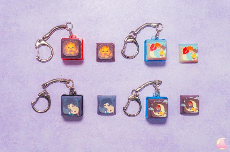 May include: Six keychains with different colorful square charms featuring cartoon characters. Each keychain has a silver metal ring and a silver chain.