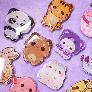 May include: A collection of ten colourful resin pins featuring various cute cartoon animals, including a panda, a tiger, a bunny, a cat, a bear, and a unicorn. The pins are all glossy and have a sparkly finish.