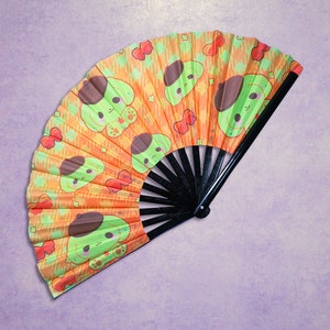 May include: A hand fan with a black handle and a colourful fabric design. The fabric is orange with green cartoon dogs wearing berets. The dogs are surrounded by red hearts and other small designs.