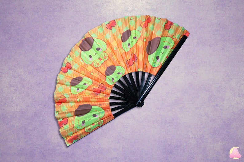 May include: A hand fan with a black handle and a colourful fabric design. The fabric is orange with green cartoon dogs wearing berets. The dogs are surrounded by red hearts and other small designs.