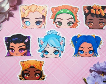May include: Set of seven colorful cartoon character stickers with cat ears. The characters have different hair colors, skin tones, and facial expressions. The stickers are printed on white paper.