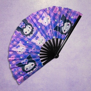 May include: A purple and pink hand fan with a black handle. The fan features a repeating pattern of cartoon characters with black eyes and white bows.