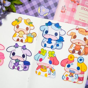 May include: Eight colorful stickers featuring cartoon cows with different accessories and food items. The stickers are on a white background with a purple and white checkered pattern in the background.