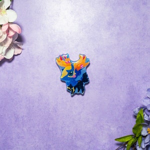 May include: A blue and yellow enamel pin featuring a cartoon character with a star on its chest and a yellow mane. The character is surrounded by a blue and black background.