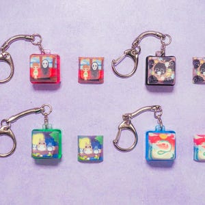 May include: Set of ten colorful keychains featuring various anime characters. Each keychain has a clear plastic charm with a different character image. The charms are attached to silver metal key rings.