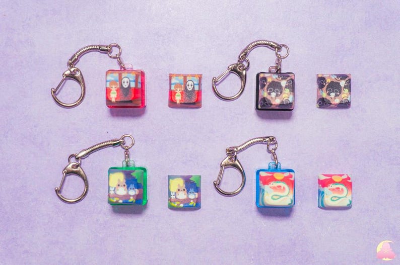 May include: Set of ten colorful keychains featuring various anime characters. Each keychain has a clear plastic charm with a different character image. The charms are attached to silver metal key rings.