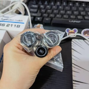 May include: A close-up of three round black push button switches. The switches have silver metal housings and are labeled "NO", "  ", and "  ".