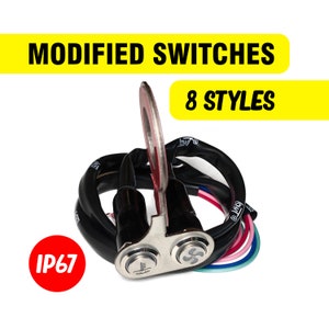Op de afbeelding: Een paar gemodificeerde waterdichte schakelaars met een zwarte behuizing en zilveren afwerking. De schakelaars hebben een ventilator- en een temperatuursymbool. De schakelaars zijn verbonden met een zwarte draad met een ringklem. De tekst "IP67" is zichtbaar in rood. De tekst "MODIFIED SWITCHES" en "8 STYLES" is zichtbaar in geel.