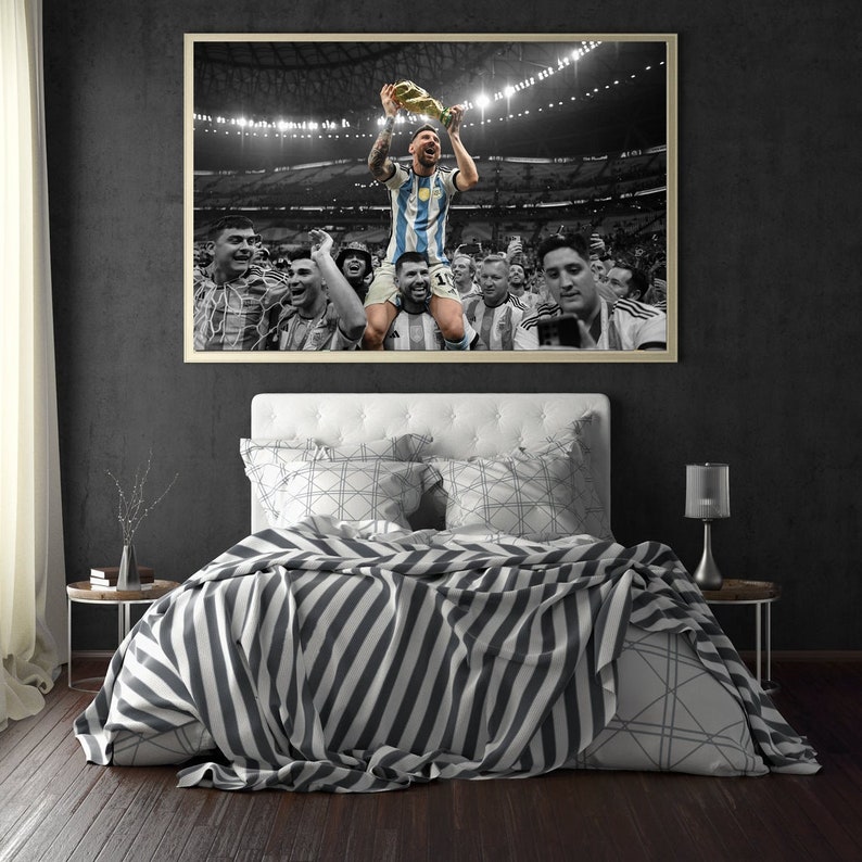 May include: A framed print of a soccer player holding a trophy, surrounded by teammates, in a stadium setting. The image is mostly black and white, with the player's jersey in blue and white stripes. The print hangs above a bed with a striped blanket.