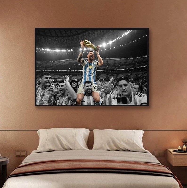 May include: Framed black and white photograph of a soccer player holding a trophy, surrounded by teammates in a stadium. The player is wearing a blue and white striped jersey. The image is displayed above a bed.